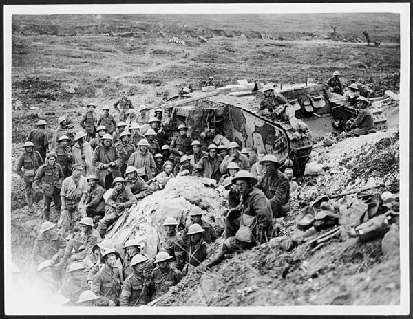 A tank is surrounded by infantrymen at Flers in France. The manner in which the soldiers are gathered together around the tank and looking directly at the camera, suggests that this could be a staged photograph taken for propaganda purposes. It is believed that this photograph was taken by John Warwick Brooke. The Battle of Flers-Courcelette formed a supplementary part in the third phase of the great Somme offensive in mid-September 1916. The battle is important because this was where tanks were first used during the conflict. Winston Churchill, then fighting as a lieutenant colonel of infantry on the Western Front, complained that Haig’s contentious decision to attack at Flers with a small number of tanks was wrong, and lamented that 'my poor 'land battleships’ have been let off prematurely on a petty scale'. [Original reads: 'OFFICIAL PHOTOGRAPHS TAKEN ON THE BRITISH WESTERN FRONT IN FRANCE. One of our Tanks at Flers.']  John Warwick Brooke. National Library of Scotland License: CC BY 4.0