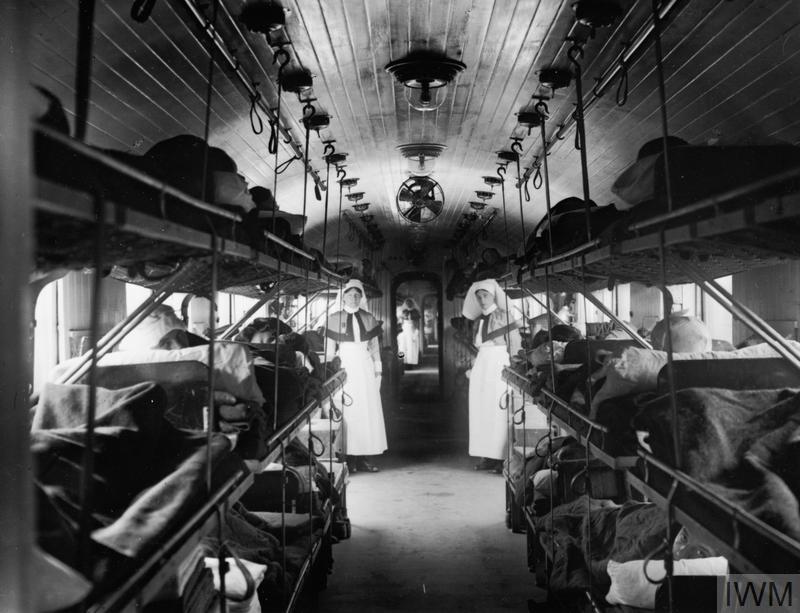 The interior of a coach of a British hospital train showing cots arranged down either side of the carriage leaving a wide central passageway in which the medical staff could work. © IWM (Q 33447)